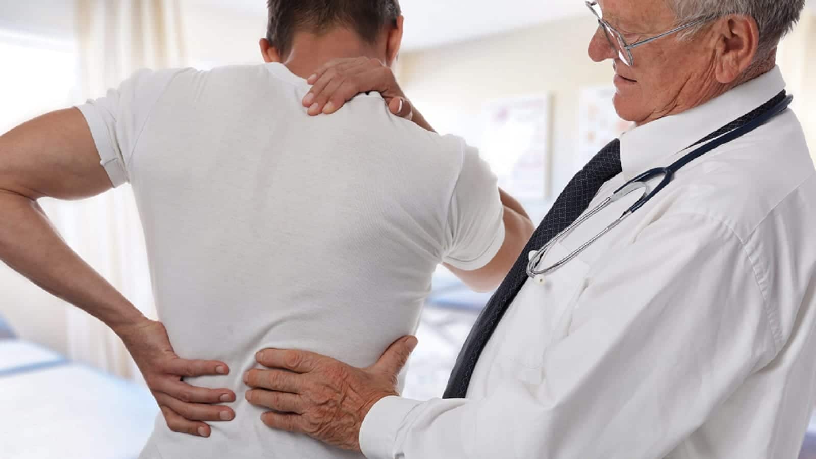 Male Doctor and patient suffering from back pain during medical exam.
